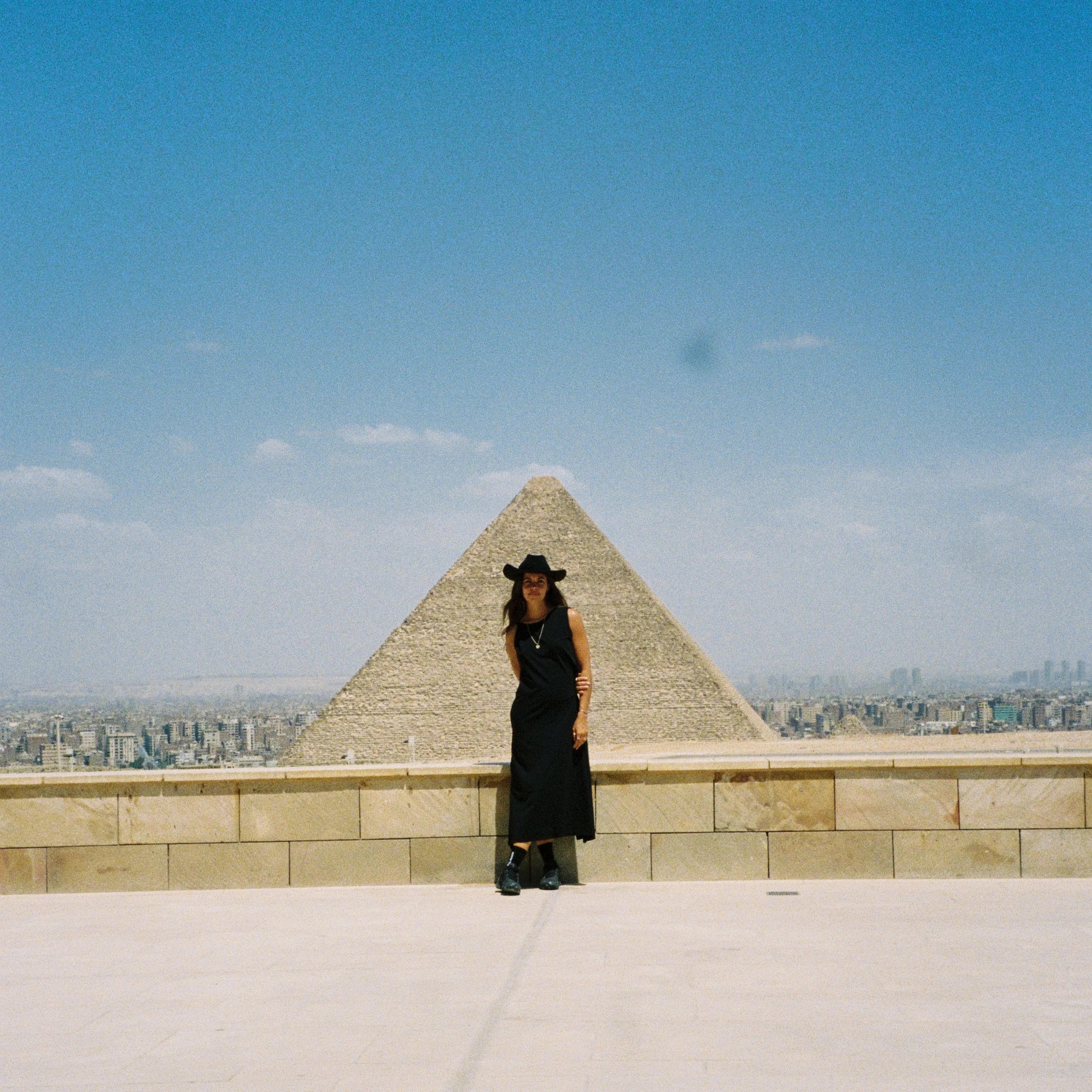 Mimi ElAshiry in a black dress standing on a rooftop with the pyramid in the background, Egypt - Stamps Tours