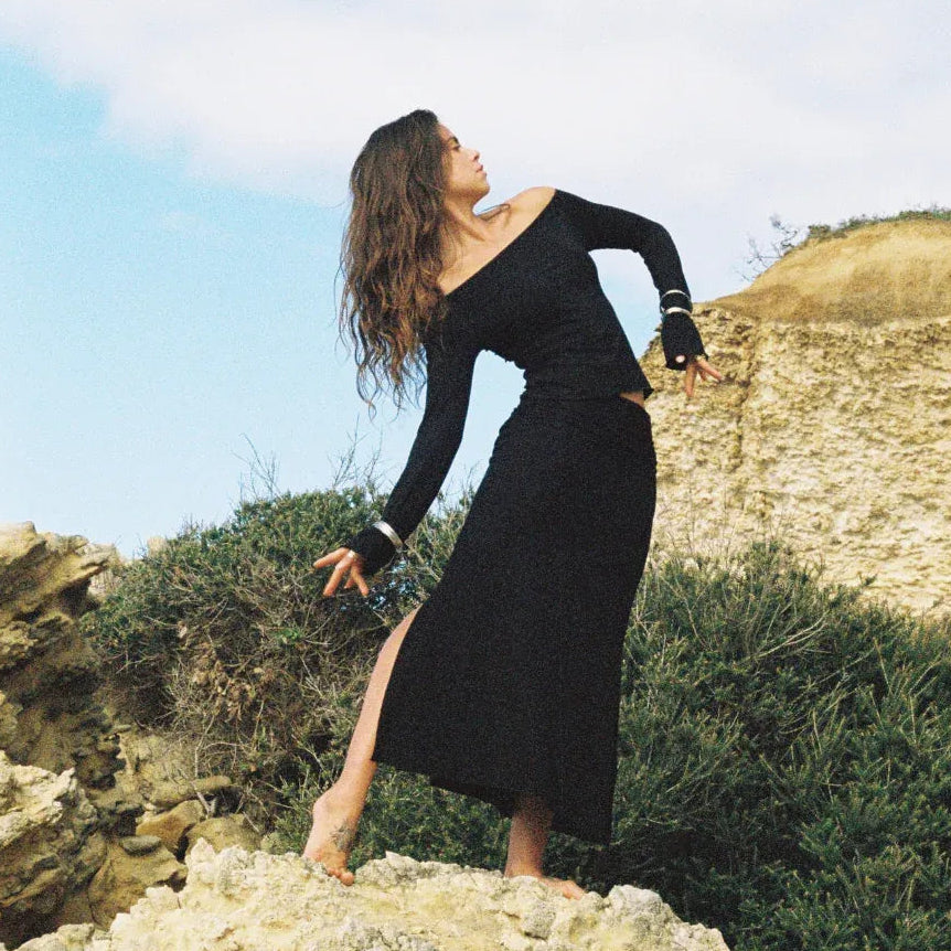 Mimi ElAshiry in a black dress standing on rocks with a scenic background - Stamps Tours